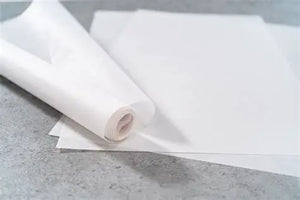 Ein aufgerolltes Blatt weißes Backpapier liegt auf einem anderen Blatt.